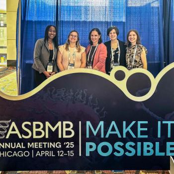 Five people stand behind an ASBMB Annual Meeting 2025 sign in Chicago, featuring the event theme "Make It Possible."