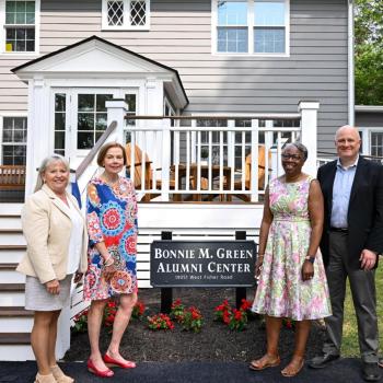Five people stand in front of the Bonnie M. Green Alumni Center, posing for a photo near the building's entrance and a sign with the center's name.