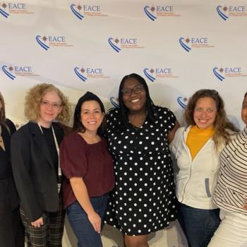 Six women standing together and smiling in front of a backdrop with EACE logos.
