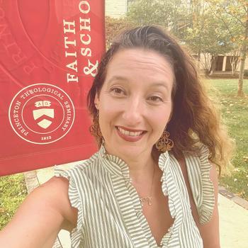 A woman smiles for a selfie in front of a Princeton Theological Seminary banner outdoors on a sunny day.