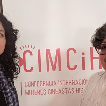 Two women stand in front of a CIMCiH banner at a conference for women filmmakers and historians.