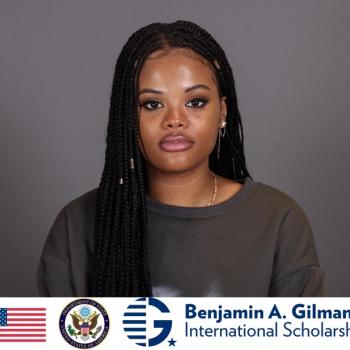 A woman with long braided hair looks at the camera against a plain background. The Benjamin A. Gilman International Scholarship logo and US symbols appear at the bottom.
