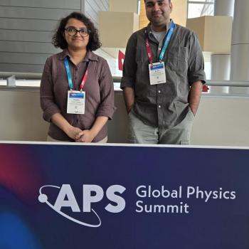 Drs. Shalini Ganguly (left) and Anish Agashe (right) stand behind a banner that reads "APS Global Physics Summit," each wearing conference badges.