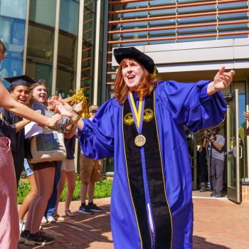 President Rhonda Phillips celebrates outside a building while a group of people clap and cheer.