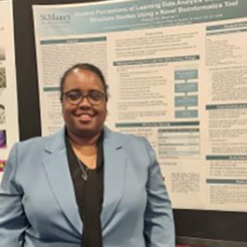 A person wearing glasses and a light blue blazer stands in front of a scientific research poster.
