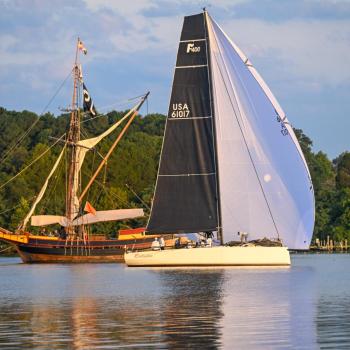 A sail boat with black and white sails passes the Maryland Dove talliship on the St. Mary's River 