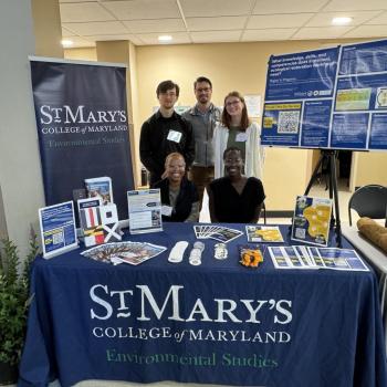 Five people pose at a St. Mary’s College of Maryland Environmental Studies booth featuring informational displays and brochures.