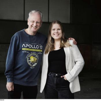 An older man in an Apollo 13 sweatshirt and a young woman in a blazer stand side-by-side, smiling for a photo.