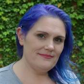 A woman with purple toned hair is pictured against an ivy covered background.