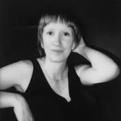 Black and white image of white woman smiling, black background.