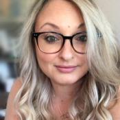Woman with long blonde wavy hair wearing glasses.