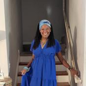 Donna Jordan wears a floor length blue dress. She has a colorful headband on. 