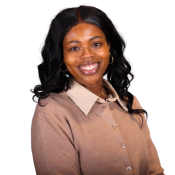 A person with long, wavy, black hair smiling warmly. They are wearing a beige button-up shirt over a cream-colored top and gold hoop earrings. The background is plain white.