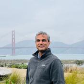 Waqar stands outdoors with the Golden Gate Bridge and cloudy skies in the background.