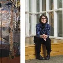 A woman with glasses, short dark hair, and a blue patterned shirt sits on a wooden bench by large windows. An abstract textile artwork is displayed on the left.