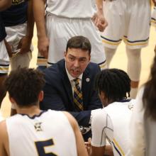 Chris Harney talking to players at halftime of men's basketball game 