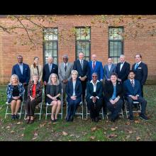 A group of people in business attire are pictured in front of brick building outdoors.