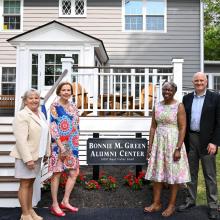 Five people stand in front of the Bonnie M. Green Alumni Center, posing for a photo near the building's entrance and a sign with the center's name.