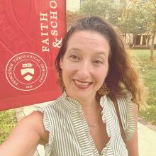 A woman smiles for a selfie in front of a Princeton Theological Seminary banner outdoors on a sunny day.
