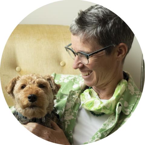 White woman with graying brown short hair looking fondly at small golden brown terrier