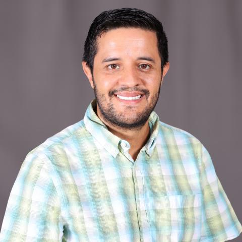 A man wearing a plaid shirt smiles.