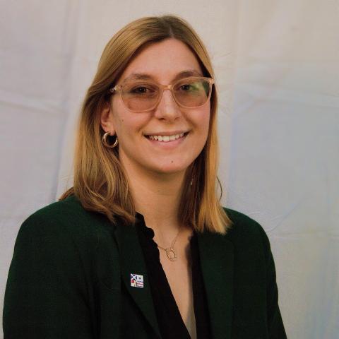 A woman wearing a dark shirt and glasses smiles.