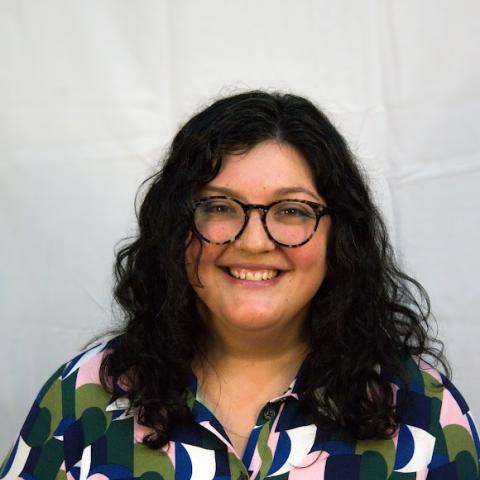 A woman with curly black hair and round brown glasses smiles at the camera.