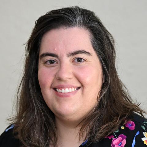 A woman with dark hair and a floral shirt smiles.