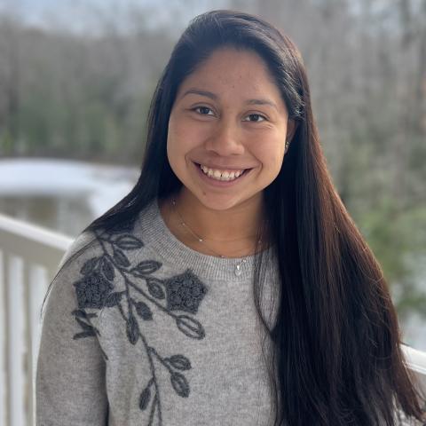 A smiling person with long, dark hair is wearing a gray sweater with a floral pattern.