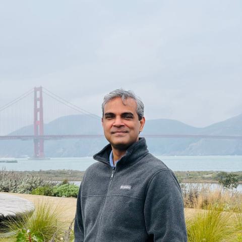 Waqar stands outdoors with the Golden Gate Bridge and cloudy skies in the background.