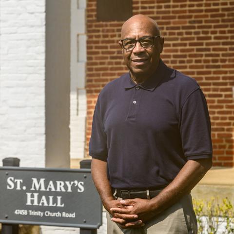 A man wearing glasses and a navy polo shirt stands outside next to a sign.