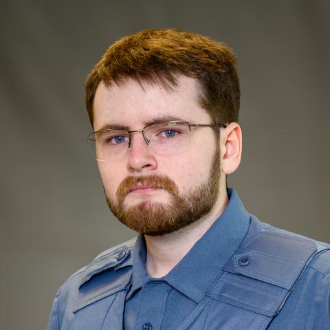 A person in a blue police uniform and glasses, wearing a badge and a name tag that reads "Walsh," stands against a plain background.