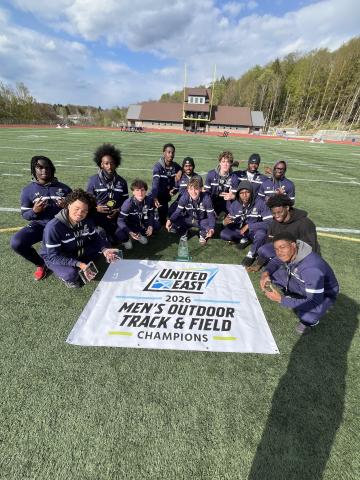 A men's track and field team poses on a field behind a banner that reads "United East 2026 Men's Outdoor Track & Field Champions."