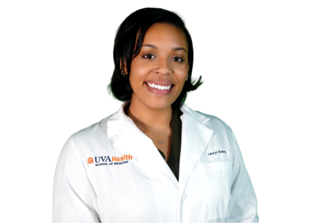 A woman wearing a white UVA Health School of Medicine lab coat stands and smiles at the camera against a white background.