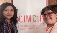Two women stand in front of a CIMCiH banner at a conference for women filmmakers and historians.