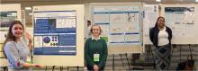 Three individuals stand next to separate research posters at a conference, each presenting scientific information with charts and text on display boards.