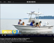 Four people examine something on a small white boat on the water during a CBS News segment about St. Mary’s College of Maryland.