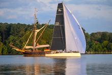 A sail boat with black and white sails passes the Maryland Dove talliship on the St. Mary's River 