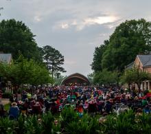 A large crowd sitting in lawn chairs facing an outdoor amphitheater stage.