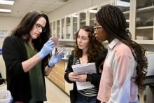 An instructor in a laboratory shows a petri dish to two students.