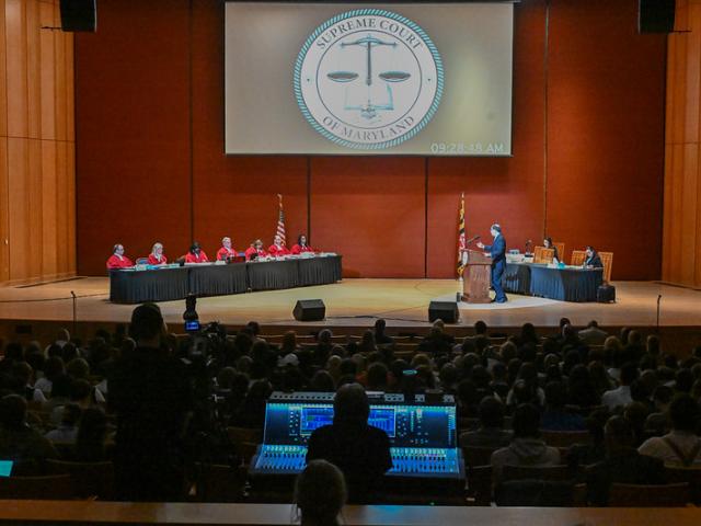 Supreme Court justices on stage hear oral arguments in front of large audience