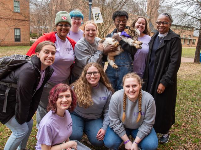 President Jordan and a group of students pose with a young goat outside on campus