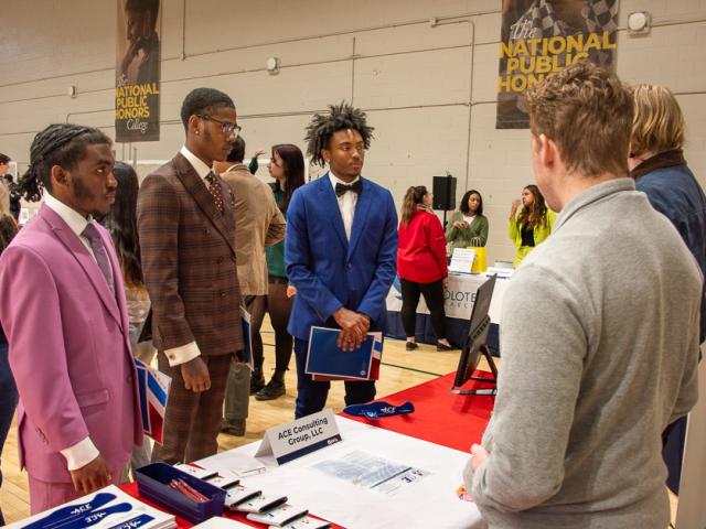 three SMCM Students stand and a booth listening to recruiters from a local consultant team  at the Spring 2024 Career and Internship Fair