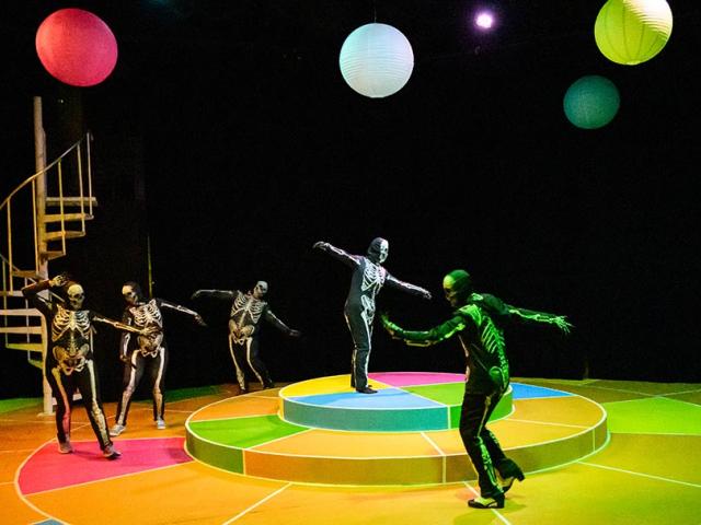 Actors dressed as skeletons dance around on colorful stage