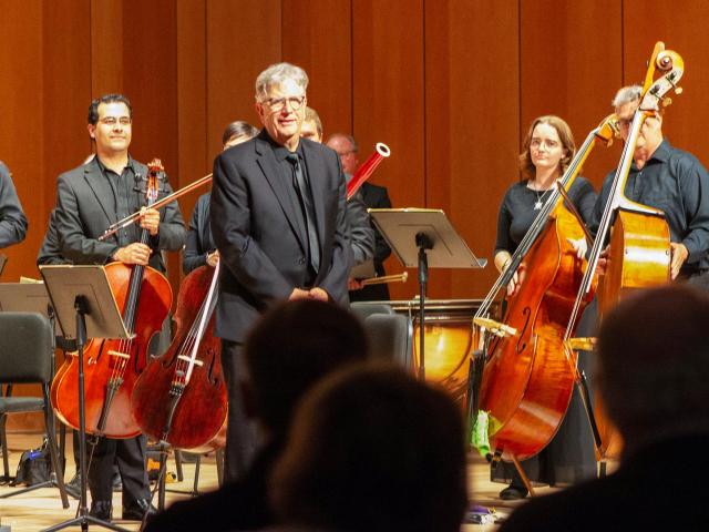 Conductor on stage in front of orchestra receiving standing ovation