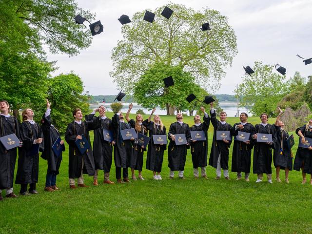 15 graduates in regalia tossing caps into the air