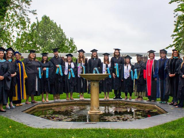 Students and faculty in caps and gowns gathered around Remembrance Garden 