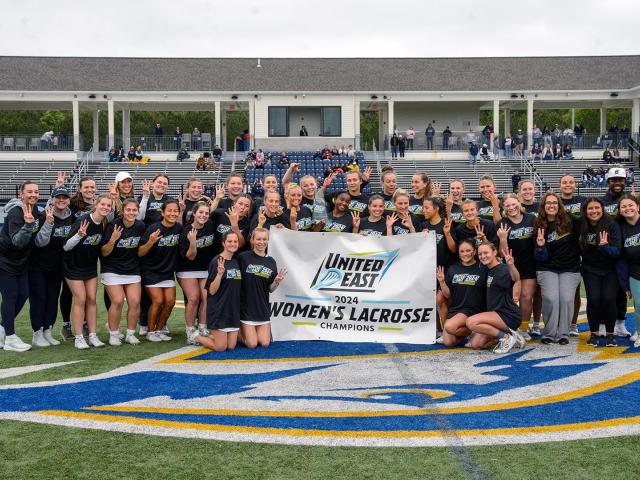 Women's lacrosse team and caches with championship banner