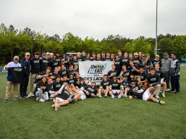 Lacrosse team and coaches with United East championship banner