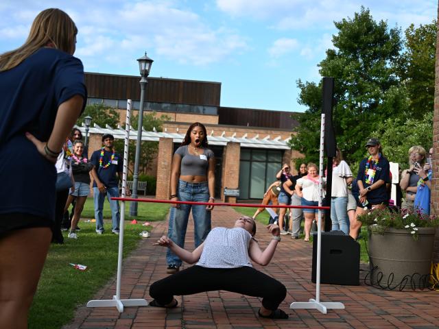 A young woman attempts to limbo under a stick while a crowd observes 